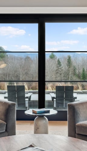 sitting room with two armchairs and a large black-framed window overlooking trees and mountains