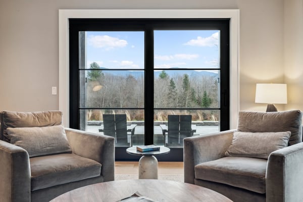 sitting room with two armchairs and a large black-framed window overlooking trees and mountains